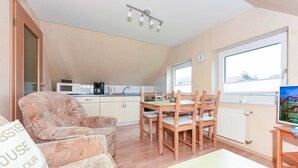 Ein gemütliches Wohnzimmer mit einer Couch, einem Holzespeisetisch mit Stühlen, einem Fernseher und einer Küchenzeile mit Mikrowelle und Spüle.