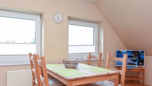 Ein Essbereich mit einem Holztisch und Stühlen, einer Wanduhr und einem Fernseher auf einem Lowboard.