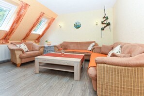 A cozy living room with a sofa set, a wooden coffee table, and a view of the outdoors through a window with curtains.