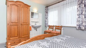 Ein Schlafzimmer mit einem hölzernen Bett, einem Schrank aus Holz, einem weißen Waschbecken und einem Fenster mit Vorhängen.