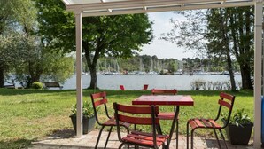 En overdækket terrasse med et bord og stole, der giver udsigt over en sø med både.