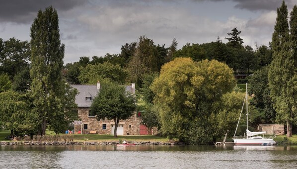 Une maison en pierre avec un quai au bord d’un lac, entourée d’arbres.