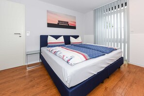 Quarto com cama, mesa de cabeceira, quadro e janela com persianas.