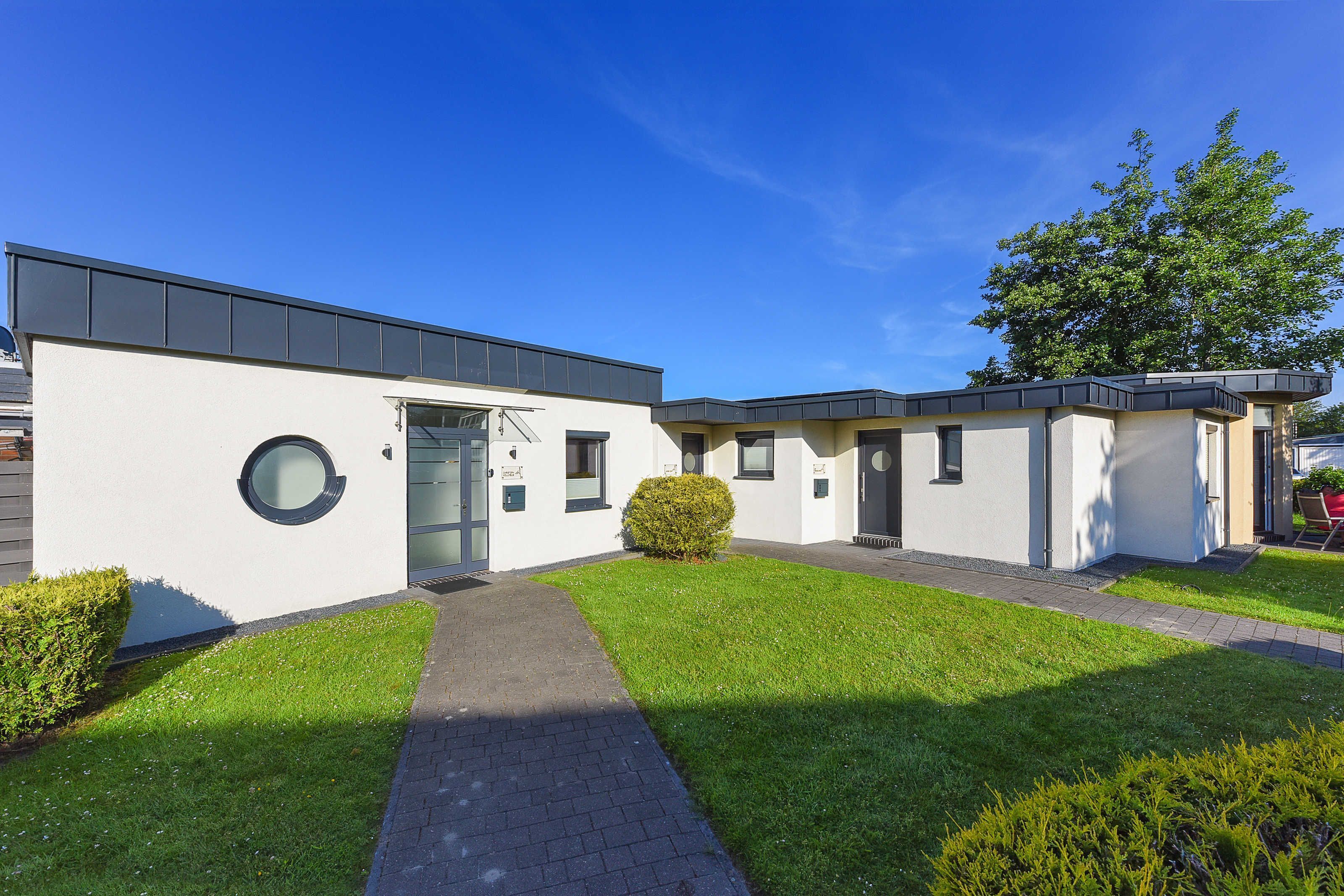 A modern building with a flat roof, a circular window, and a well-maintained lawn.