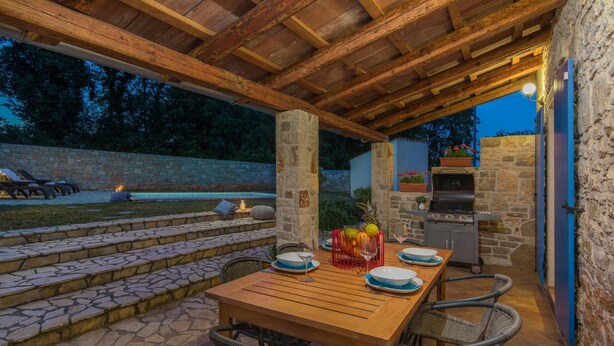 An outdoor patio with stone steps, a wooden table set for dining, wicker chairs, and a stone wall.