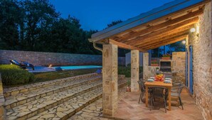 An outdoor patio with stone steps leading to a covered seating area, a pool, and a stone wall.