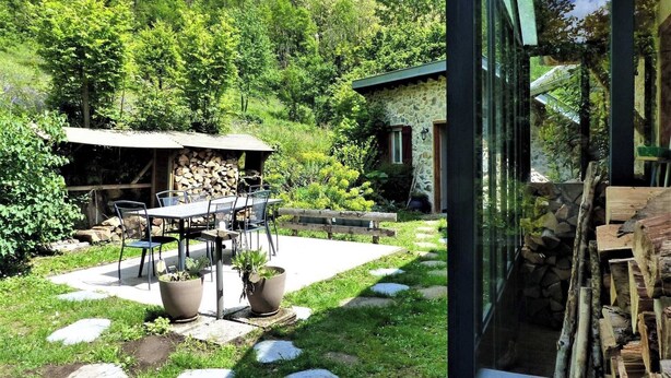 A patio with a table and chairs, a stone wall, and a wooden deck. - Gîte de Fontainebleau (Vicdessos)