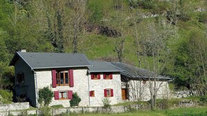 A stone house with red shutters, a sloped roof, and a stone wall foundation. - Gîte de Fontainebleau (Vicdessos)