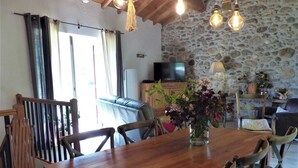 A wooden dining table with chairs, a television, and a stone wall. - Gîte de Fontainebleau (Vicdessos)