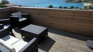 Una terraza de madera con mobiliario de mimbre que da a una playa y al mar.