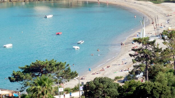Una playa costera con barcos, gente y edificios al fondo.