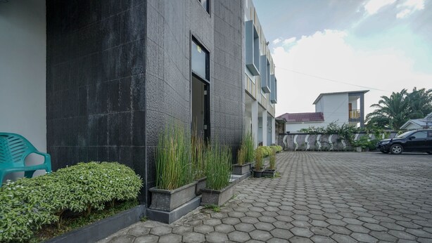 A modern building with a paved walkway, potted plants, and a parked car. - Hotel O Green Palm Kostel Syariah (Lubuklinggau)