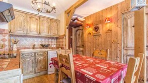 A rustic kitchen with wooden cabinets, a dining table with a red tablecloth, and a chandelier. - The charm of an alpine chalet, an ideal location for sport and shopping (Mont-de-Lans)