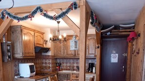 A cozy kitchen with wooden cabinets, a dining table with chairs, and a microwave. - The charm of an alpine chalet, an ideal location for sport and shopping (Mont-de-Lans)