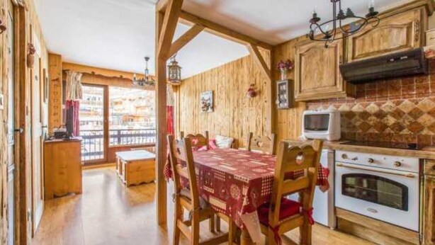 A wooden interior with a dining table, chairs, a kitchen with a stove, and a balcony with a view. - The charm of an alpine chalet, an ideal location for sport and shopping (Mont-de-Lans)
