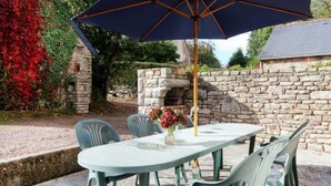 Une terrasse avec une table et des chaises, un parasol et un mur en pierre.