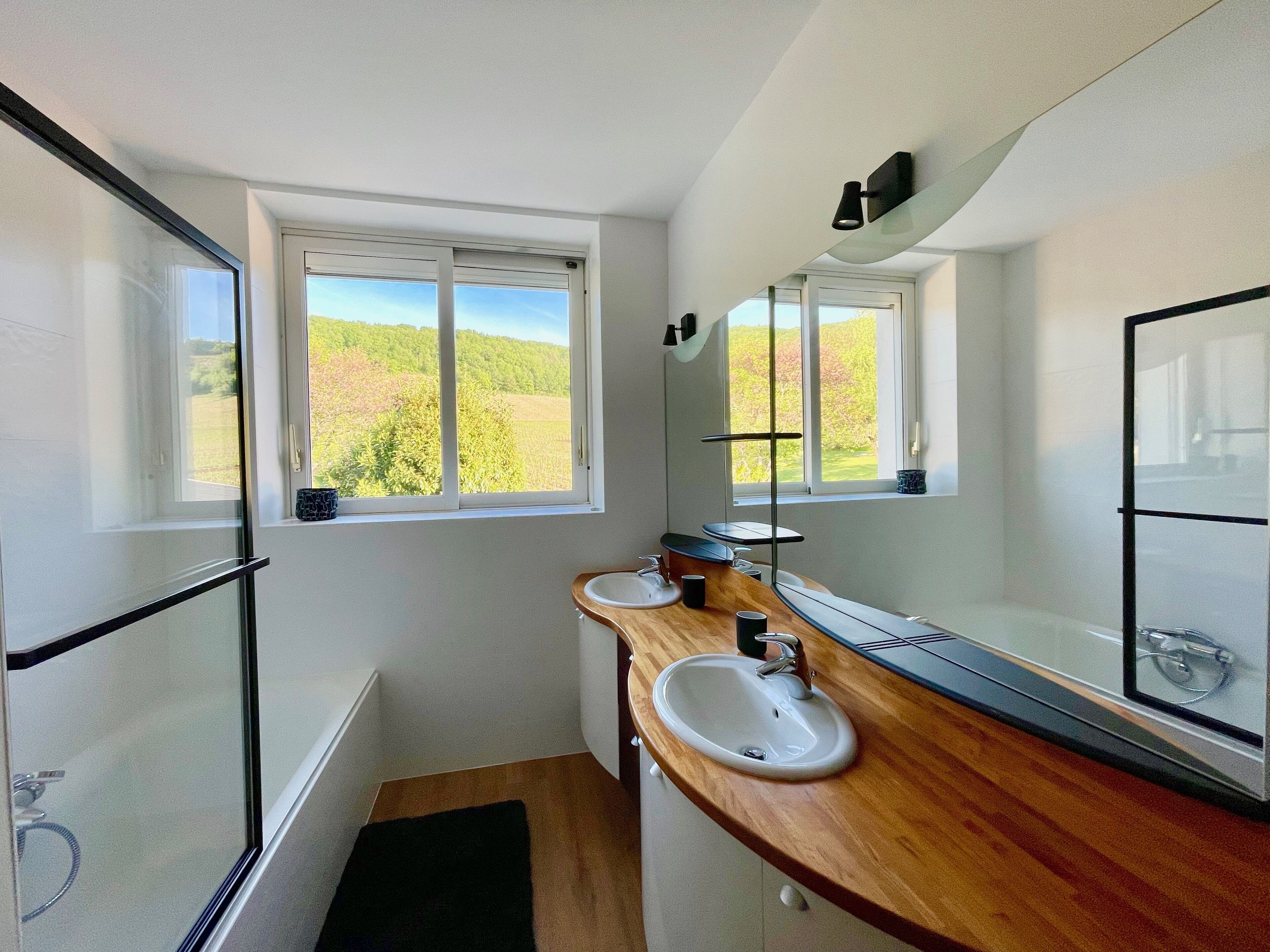A bathroom with a shower, two sinks, a window, and a mirror.