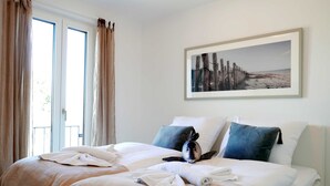 Ein Hotelzimmer mit zwei Betten, einem großen Fenster mit Vorhängen, einem gerahmten Bild an der Wand und einem Handtuch auf dem Bett.
