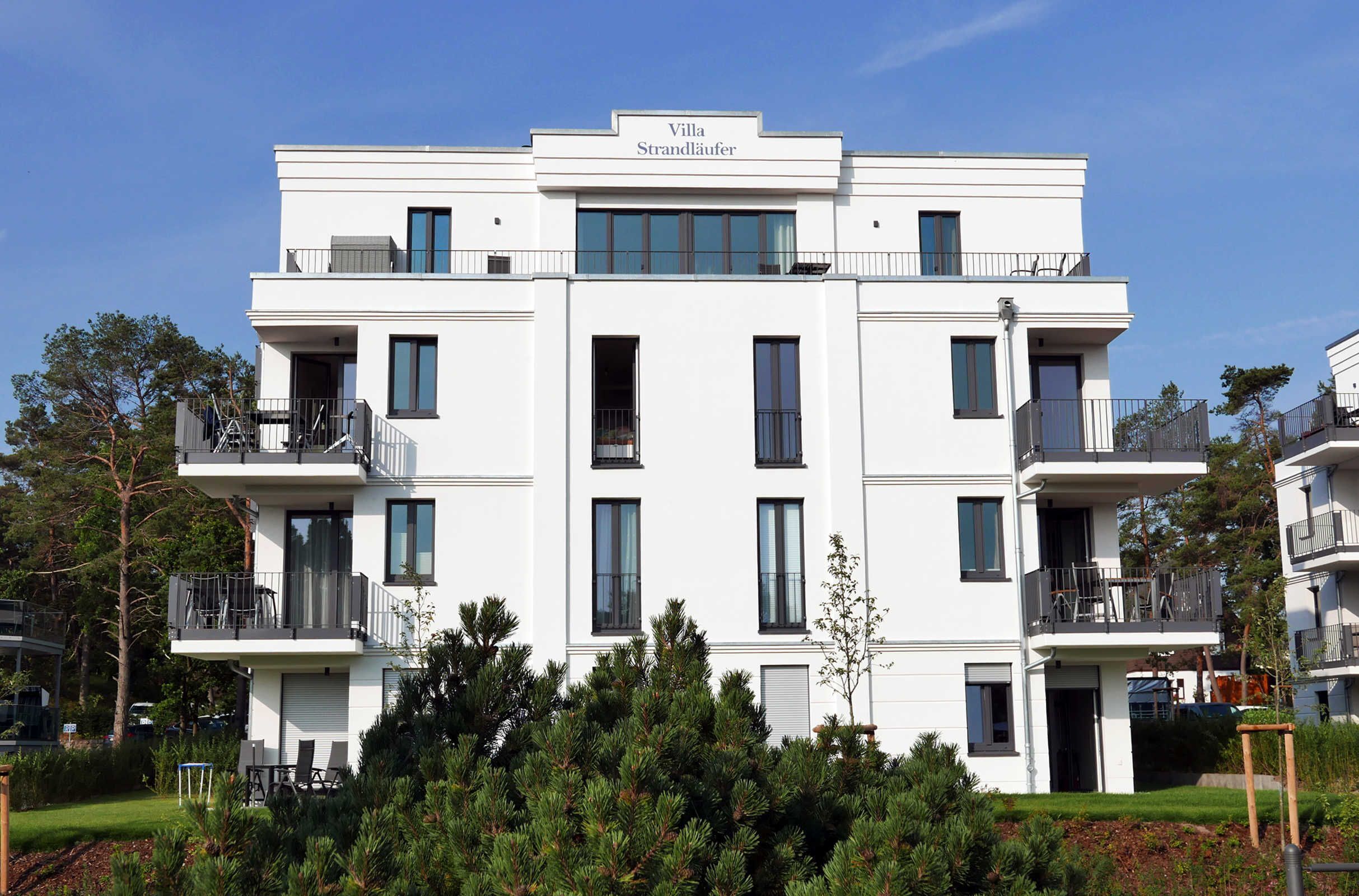 Ein modernes Mehrfamilienhaus namens Villa Strandlauer mit Balkonen, großen Fenstern und einem gepflegten Garten.