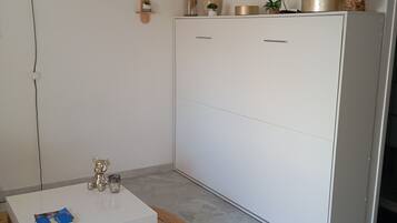 Un salon moderne avec un canapé blanc, une table basse, un téléviseur fixé au mur et un grand meuble.