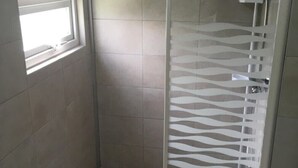 Une douche avec une porte en verre, une fenêtre et des murs carrelés.