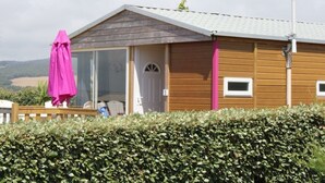 Une cabane en bois avec une porte en verre, un parapluie rose et une vue sur la campagne.