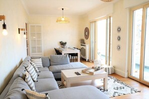Un salon moderne avec un canapé d’angle gris, une table basse blanche et un coin repas comprenant une table et des chaises blanches.