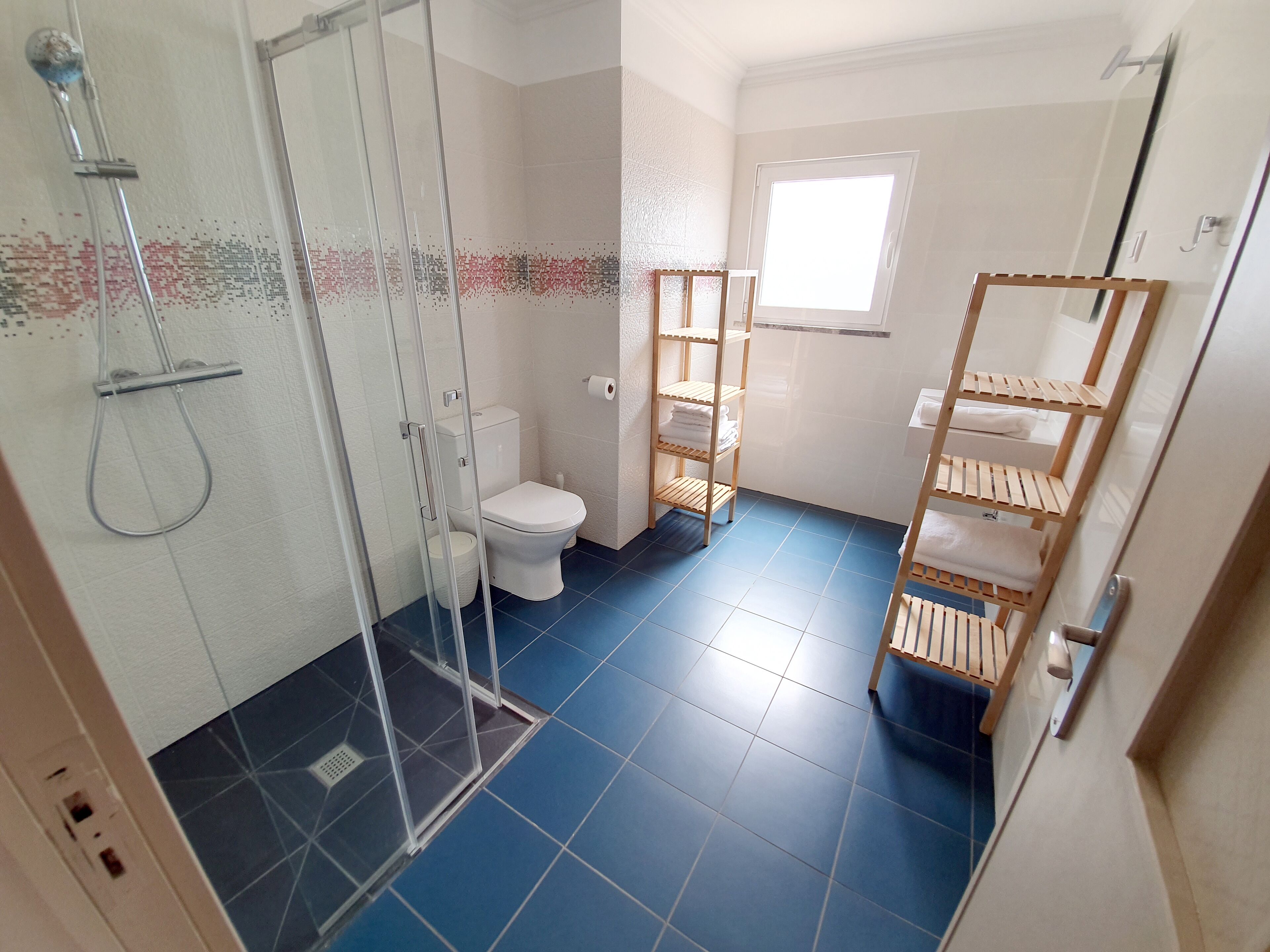 A bathroom with a shower, toilet, and wooden shelves.