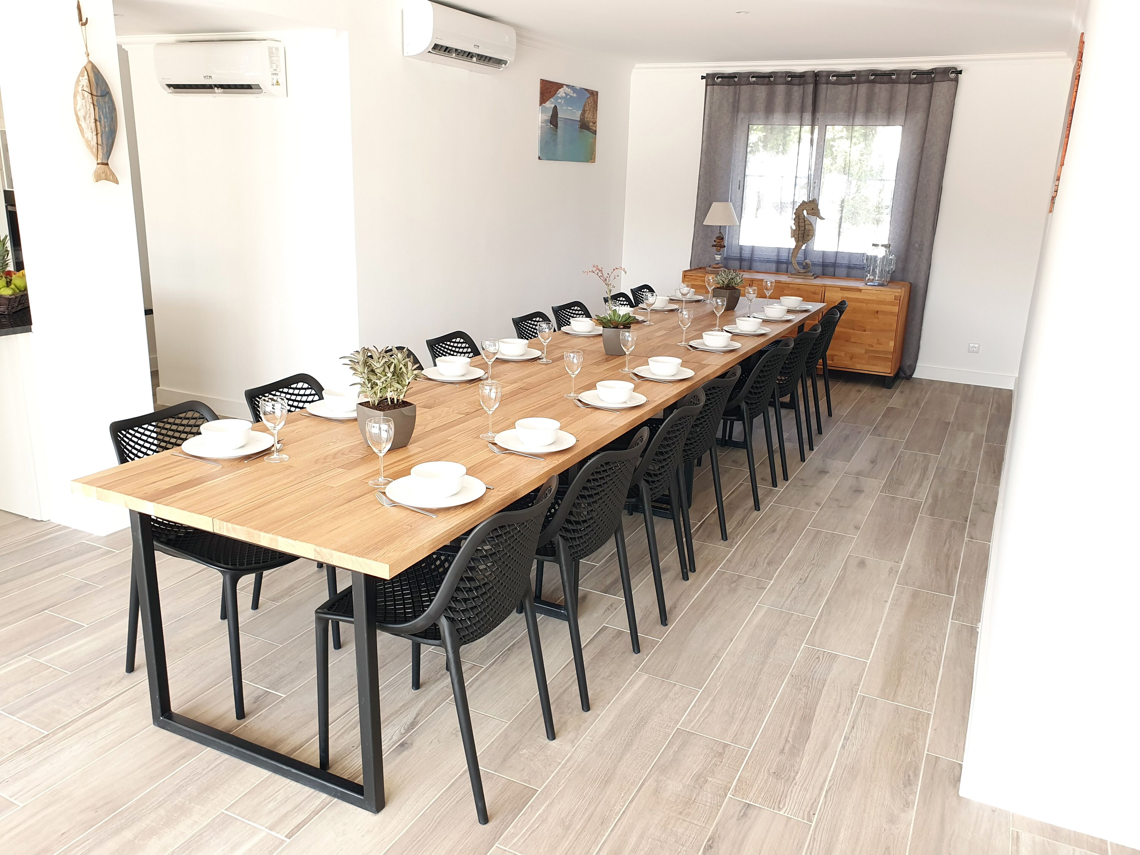 A dining area with a long wooden table set for a meal, surrounded by black chairs.