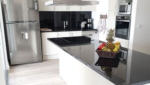 Een moderne keuken met witte kastjes, roestvrijstalen apparatuur en een centraal keukenblok met een fruitmand.