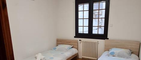 Une petite pièce propre, avec deux lits en bois, un radiateur et une fenêtre donnant sur l’extérieur.