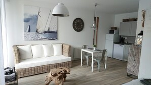 Um espaço de estar moderno com sofá branco, mesa de jantar e cadeiras, área de cozinha com eletrodomésticos e um relógio grande na parede.