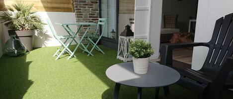 Un patio con césped artificial, una mesa redonda, una planta en maceta y mobiliario de exterior.