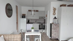 Cozinha compacta com armários brancos, micro-ondas e máquina de lavar louça. Há uma mesa de jantar com cadeiras e um pequeno vaso de planta.