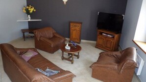 Un salon avec deux canapés en cuir marron, une table basse en bois, un meuble pour la télévision avec un écran plat, et un buffet.
