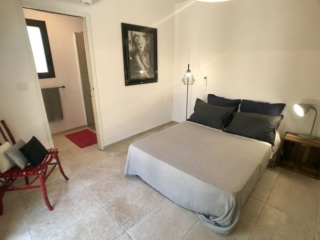 Una camera da letto con un letto, una sedia, un comodino, una lampada da terra e un quadro appeso al muro.