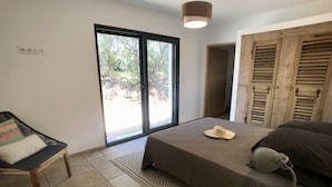 Une chambre à coucher comprenant un lit, une chaise, un bureau, une lampe et une porte coulissante donnant sur un espace extérieur.