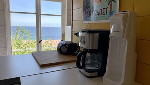 A kitchen with a coffee maker, a water dispenser, and a view of the sea through a window. - Maison pieds dans l'eau, vue mer dans une calanque 83220 Le PRADET ( Var) (Le Pradet)