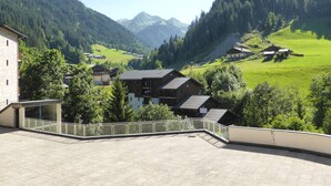 Eine gebirgige Landschaft mit Gebäuden, darunter ein Steinhaus und ein modernes Gebäude mit Balkon.