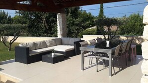 Eine Außenpatio mit einer Eckcouch, einem Esstisch mit Stühlen und einem Blumentopf.