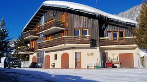 Een meerlaags houten gebouw met balkons, een overdekte ingang en een met sneeuw bedekt dak.