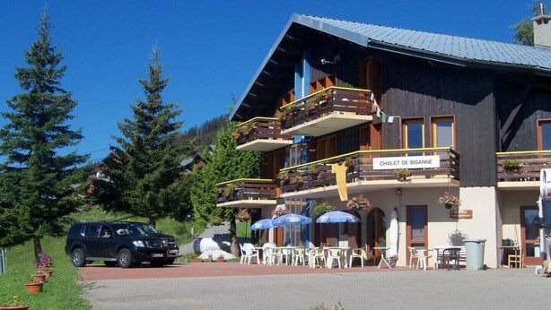 Een chalet met buiten zitplaatsen en een bord waarop staat 'CHALET DE BISANNE'.