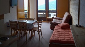 A room with a table, chairs, a sofa, and a TV. There are two windows with a view of mountains. - AT THE MOUNTAIN RENTED APARTMENT 5 PEOPLE THE ROC OF THE WIND (Villard-Sur-Doron)
