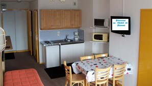 A compact kitchen with a refrigerator, microwave, and stove. There is a dining table with chairs and a television on the wall. - AT THE MOUNTAIN RENTED APARTMENT 5 PEOPLE THE ROC OF THE WIND (Villard-Sur-Doron)