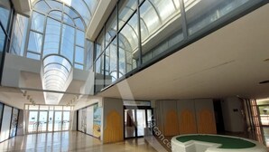 Tilava aula, jossa on korkea katto, suuret ikkunat ja vastaanottotiski.
