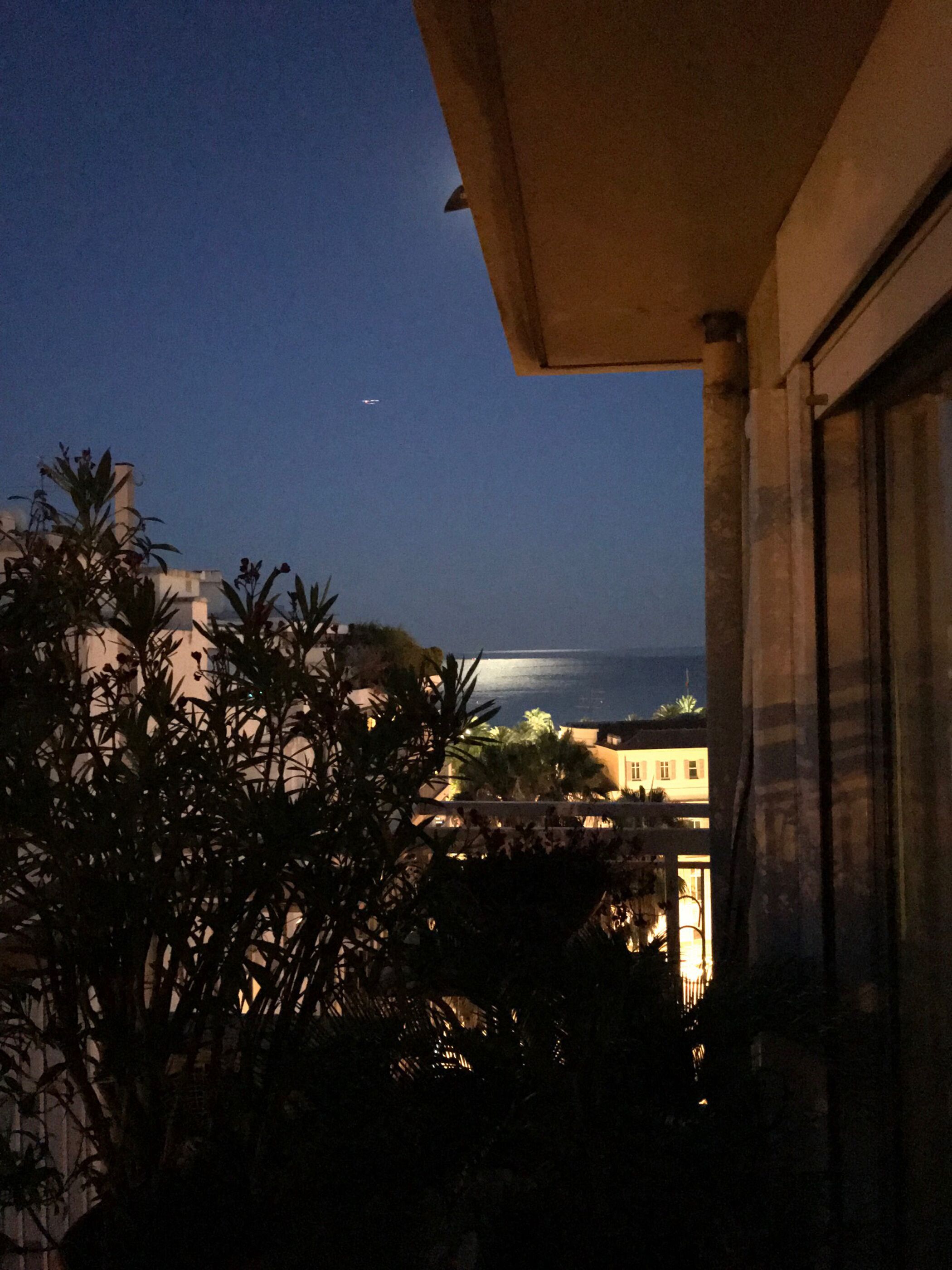 ’s Nachtzicht vanaf een balkon met uitzicht op een wateroppervlak en een vliegtuig in de verte.