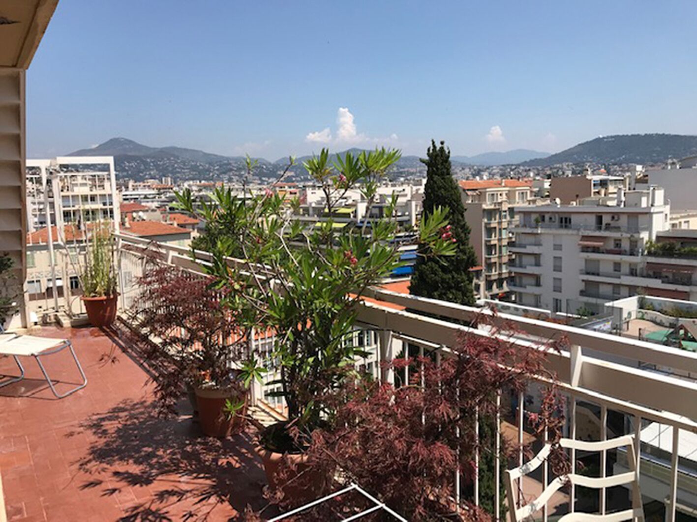 A balcony with potted plants and a view of a cityscape with buildings and mountains in the distance.