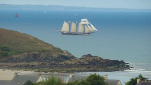 A coastal scene with a sailing ship in the distance, rocky shoreline, and a view of the sea. - panoramic sea view chalet, chalet club 8 (Plomodiern)