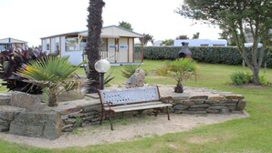 A garden with a stone bench, palm trees, and a small building with a porch. - panoramic sea view chalet, chalet club 8 (Plomodiern)