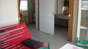 Una stanza con un divano rosso, una poltrona verde, un letto con testiera bianca e un soffitto in legno.